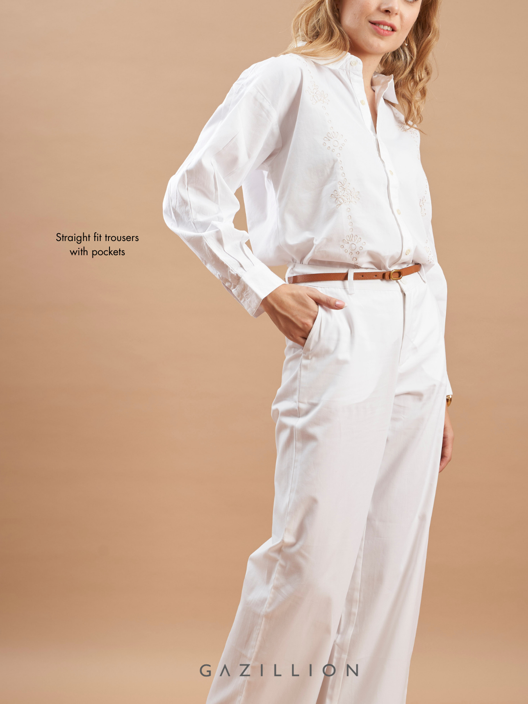Woman wearing a white shirt and pants with a brown belt on a beige background.