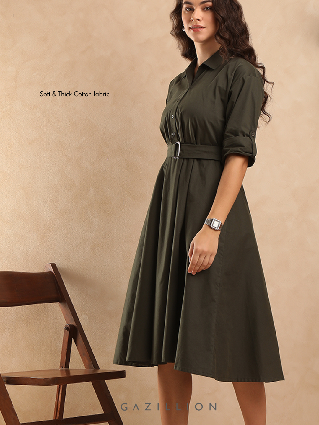 Woman wearing a green dress with a belt, standing against a beige background.