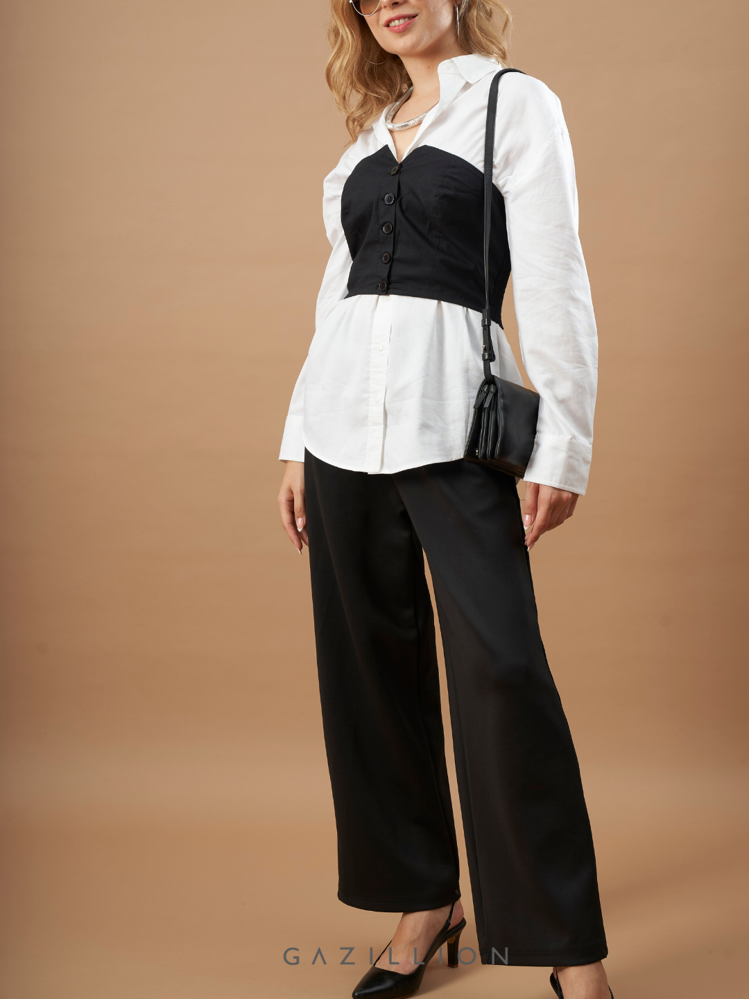 Woman wearing a white blouse, black top, and black pants against a brown background