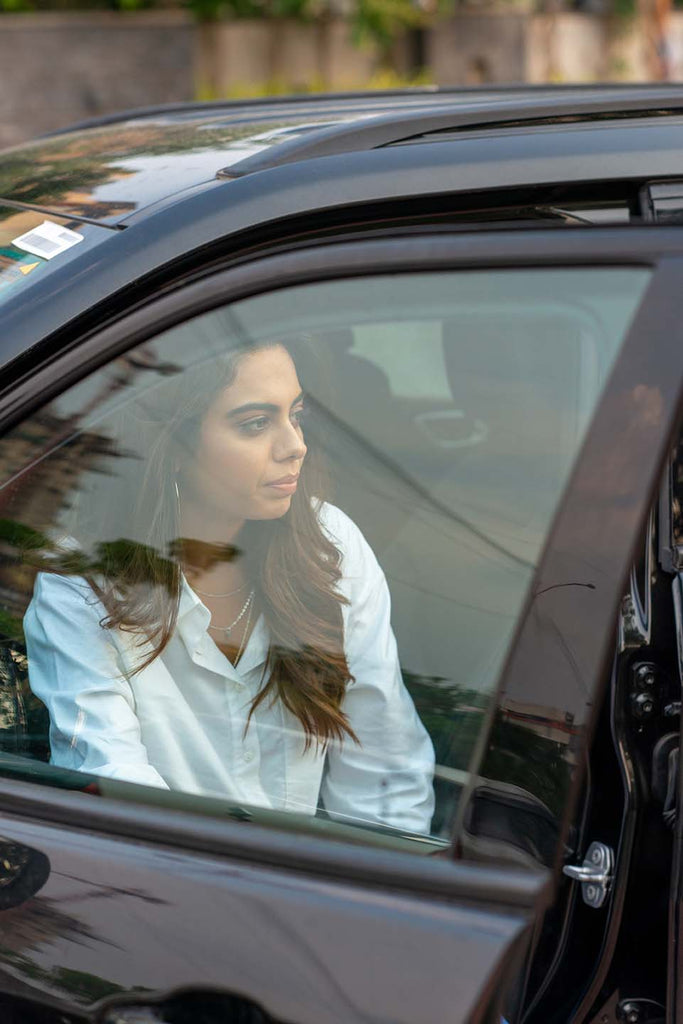 A Woman sitting in a car wearing a Gazillion White Oxford Oversized Shirt teamed with delicate necklaces