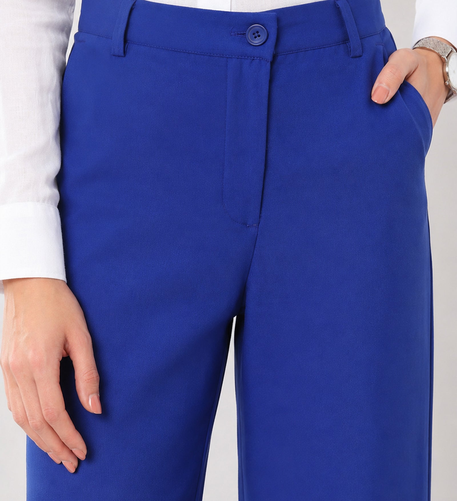 Close-up of Glin royal blue cotton pants waistband, belt loops, button fly and structured front pleat