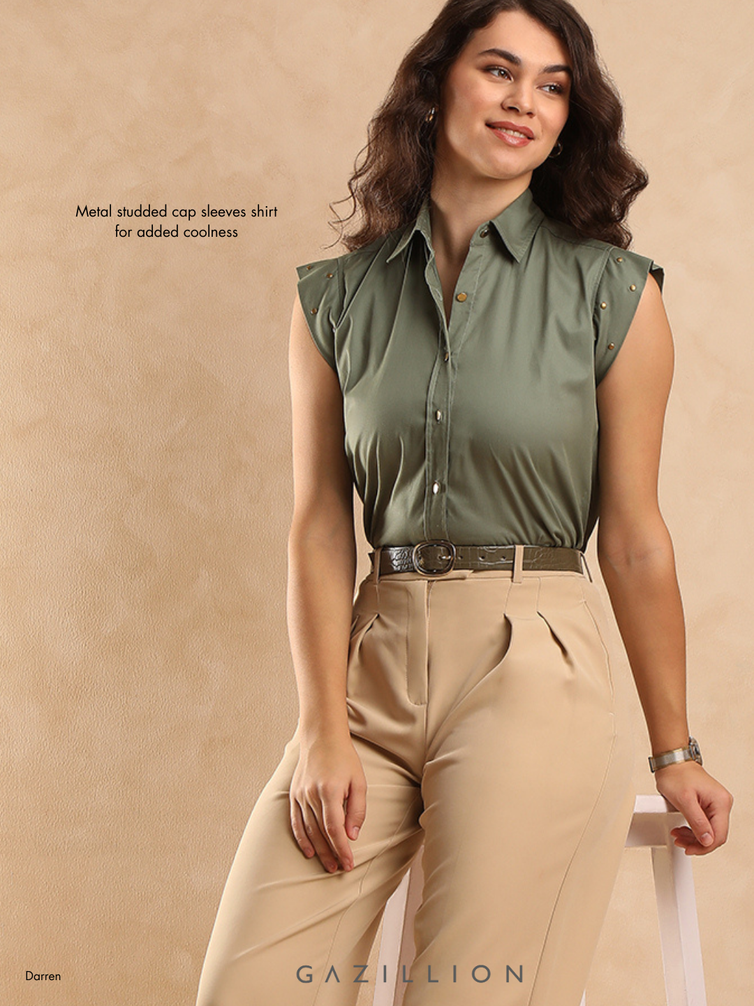 Woman wearing a green sleeveless shirt with metal studs and beige pants on a beige background